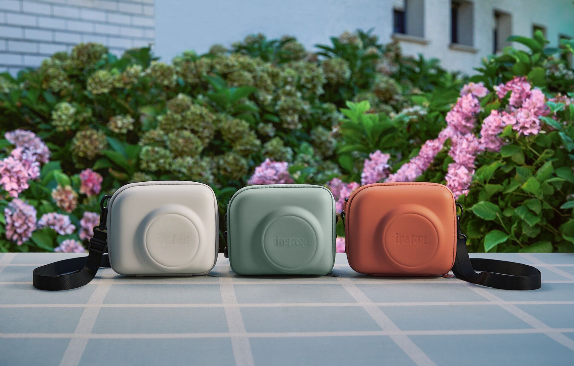 Pouzdra ve třech barvách pro fotoaparáty Fujifilm instax SQUARE 2 před květinami